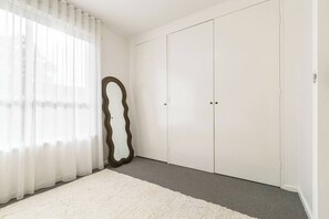 Une chambre dotée d’une grande armoire, d’un miroir et de rideaux en voile.