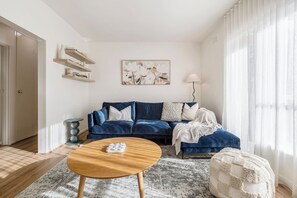 A living room with a blue sofa, a wooden coffee table, and a patterned rug. - Velvet Bloom Sunlit Comfort by Parks and Trails (Kew)