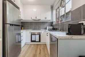 A modern kitchen with white cabinets, a stainless steel refrigerator, a built-in oven, and a coffee machine. - Velvet Bloom Sunlit Comfort by Parks and Trails (Kew)