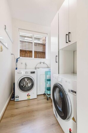 A laundry room with two washing machines, a sink, and a window with a view of a wooden fence. - Velvet Bloom Sunlit Comfort by Parks and Trails (Kew)