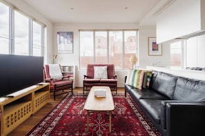 Ein Wohnzimmer mit einem großen Flachbildfernseher, einem roten Sessel, einem schwarzen Ledersofa und einem roten Teppich mit Muster.