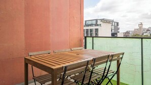 Mesa y sillas de madera en un balcón con vista a la ciudad.
