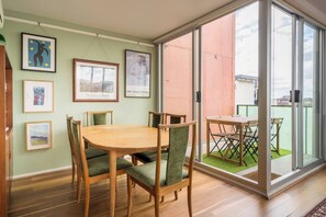 A dining area with a round table and chairs, framed artwork on the walls, and a sliding glass door leading to an outdoor space. - Garnet Gallery A Vintage Stay near Dining and Museum (Fitzroy)