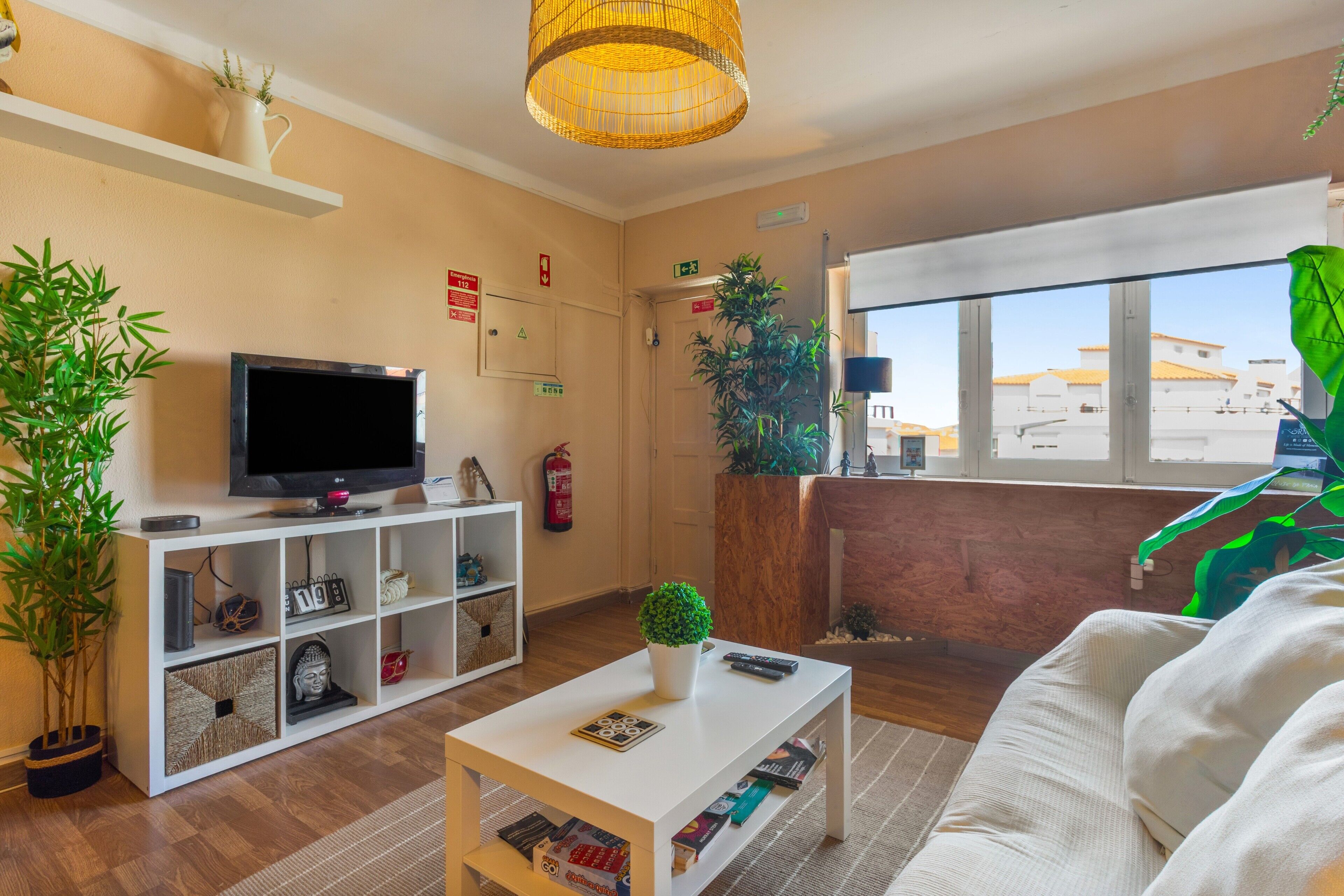 Ein Wohnzimmer mit Fernseher, einem weißen Sofa, einem Couchtisch und einem großen Fenster mit Blick auf Gebäude.