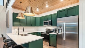 Una cucina moderna con mobili verdi, elettrodomestici in acciaio inossidabile e un'isola centrale con sgabelli da bar.