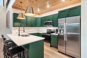 A modern kitchen with green cabinets, stainless steel appliances, and a central island with bar stools. - Modern Cabin | Near Dollywood | Hot tub | Arcade (Sevierville)