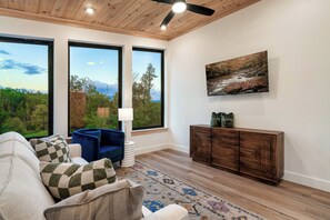 A modern living room with a large window, a flat-screen TV, a sofa, and a patterned rug. - Modern Cabin | Near Dollywood | Hot tub | Arcade (Sevierville)