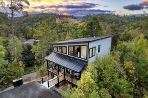A modern two-story house with a balcony, surrounded by dense forest. - Modern Cabin | Near Dollywood | Hot tub | Arcade (Sevierville)