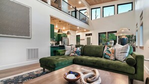 Un soggiorno moderno con un divano angolare verde, un tavolino in legno e una cucina sullo sfondo.