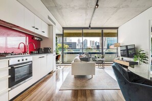 Eine moderne Küche mit roter Spritzschutzwand, ein Essbereich mit einer Couch und einem Fernseher sowie ein Balkon mit Blick auf die Stadt.