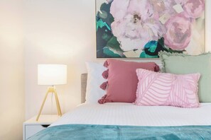 Ein Schlafzimmer mit einem Bett, einer Nachttischlampe und einem großen floralen Kunstwerk an der Wand.
