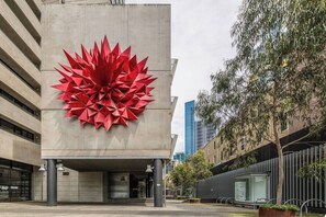 Ein modernes Gebäude mit einer großen, roten, geometrischen Skulptur an der Fassade.