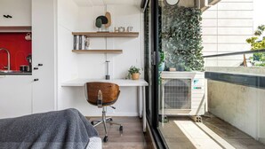 A compact living space with a kitchenette, a wooden chair, a small desk with shelves, and a view of the city through a window. - Southbank Vista Modern Retreat with Pool and Rooftop (Southbank)