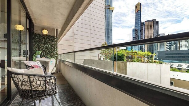 A balcony with a chair and a small table, a glass door, and a view of city buildings. - Southbank Vista Modern Retreat with Pool and Rooftop (Southbank)