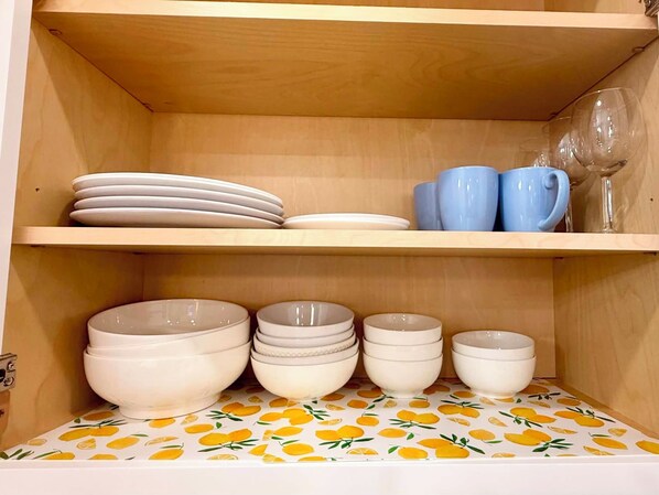 Una estantería de cocina con platos blancos, cuencos y tazas azules.