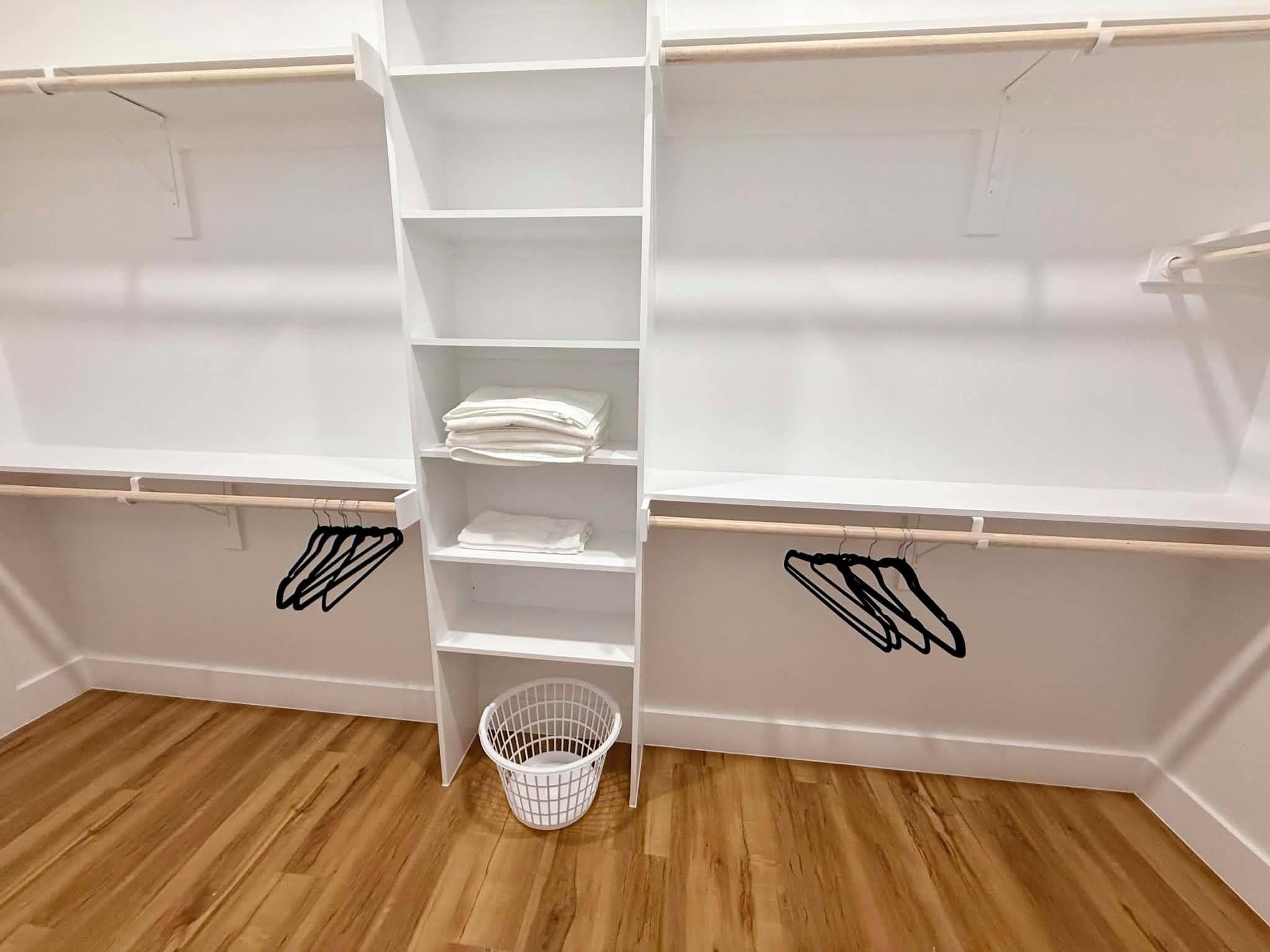 A closet with multiple shelves and a hanging rod, a white basket, and a wooden floor.