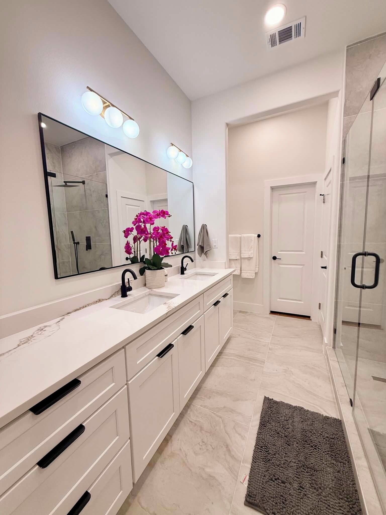 A modern bathroom with a large mirror, two sinks, a shower, and a glass door.