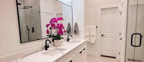 A modern bathroom with a large mirror, two sinks, a shower, and a glass door.