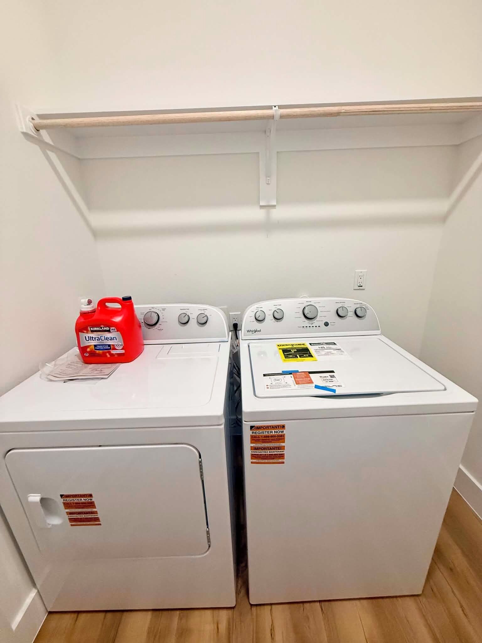 Two front-loading washing machines with a shelf above them.