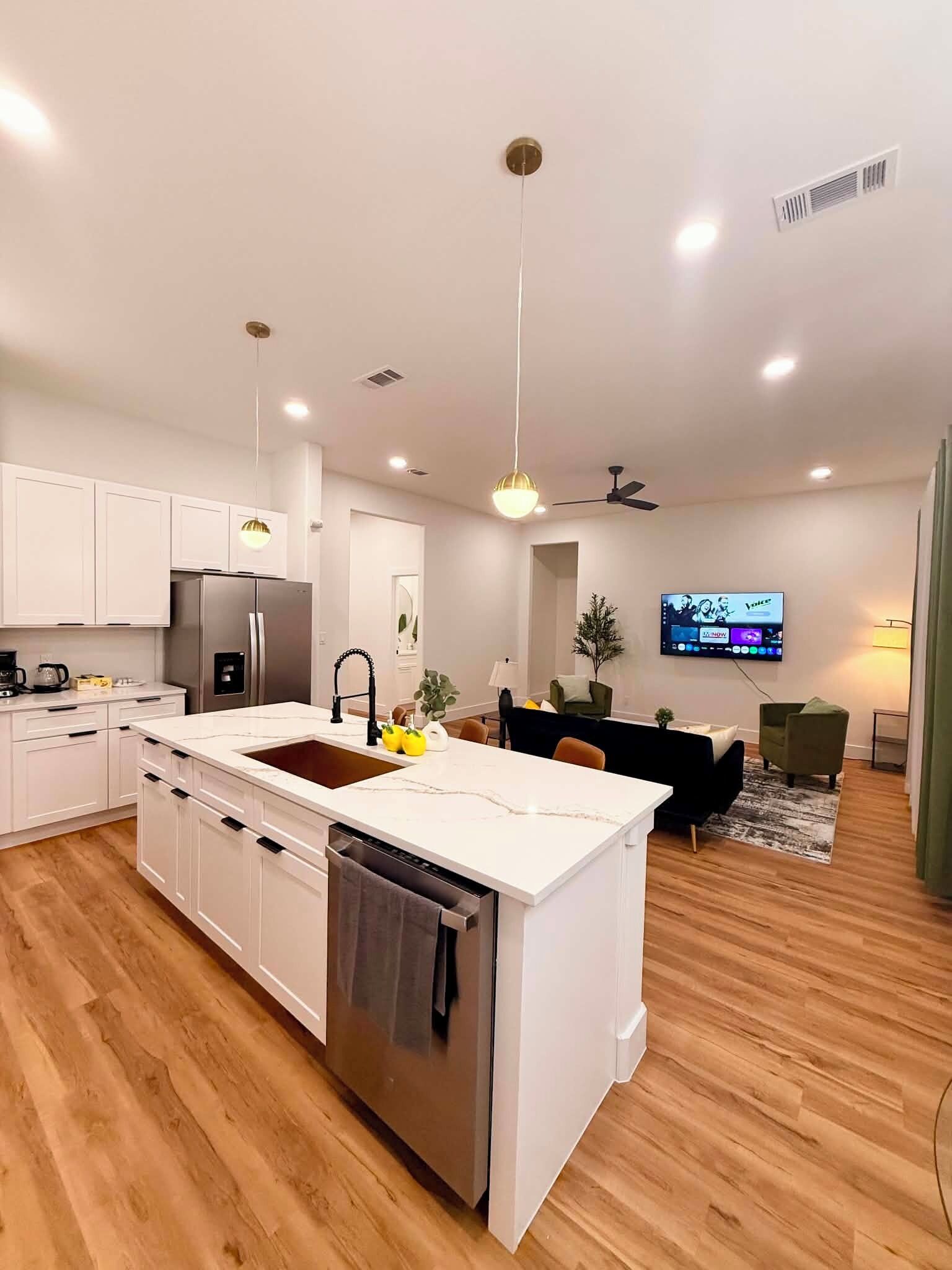 A modern kitchen with a central island, stainless steel appliances, and a flat-screen TV mounted on the wall.