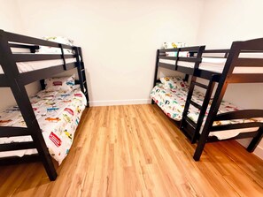 A room with two bunk beds, wooden flooring, and plain walls. - New Built House 4 Bedroom/ 2.5 Bathroom/ 4mi to AT&T/Six Flags/Rangers (Grand Prairie)