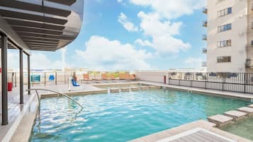 A rooftop pool area with lounge chairs and a view of the city skyline.