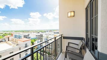 A balcony with a view of a cityscape, a seating area, and a wall-mounted light fixture.