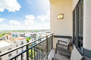 Ein Balkon mit Blick auf eine Stadtlandschaft, einer Sitzecke und einer Wandleuchte.