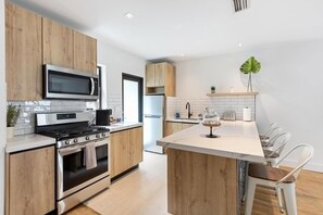 Uma cozinha moderna com armários de madeira, eletrodomésticos de aço inoxidável, uma ilha central com banquetas e vista para a área de jantar adjacente.