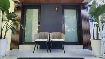 A modern entrance with two chairs, a wooden ceiling, and a black door with frosted glass panels.