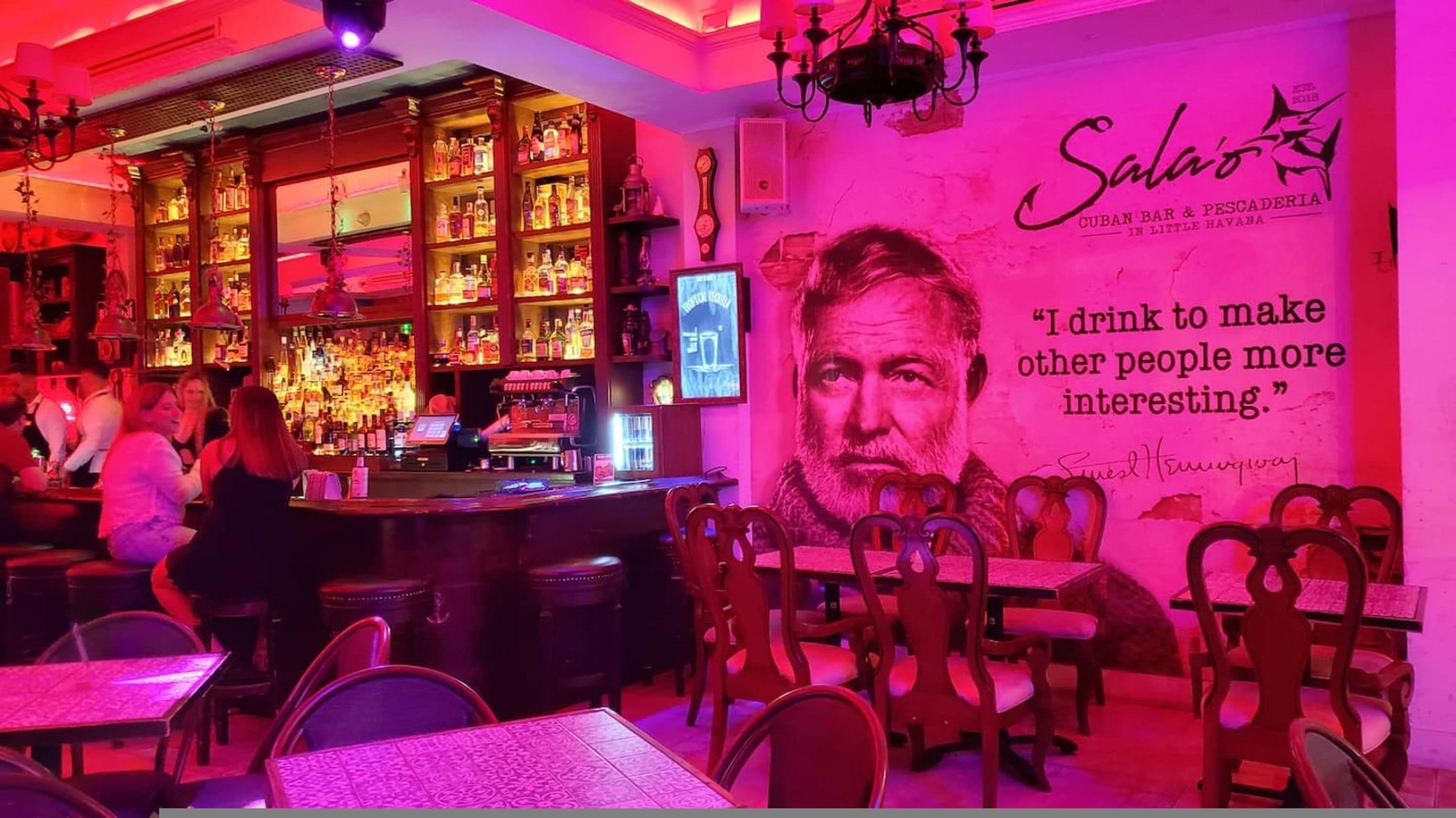 A bar area with shelves of bottles, a bar counter, and a wall with a quote and a signature.