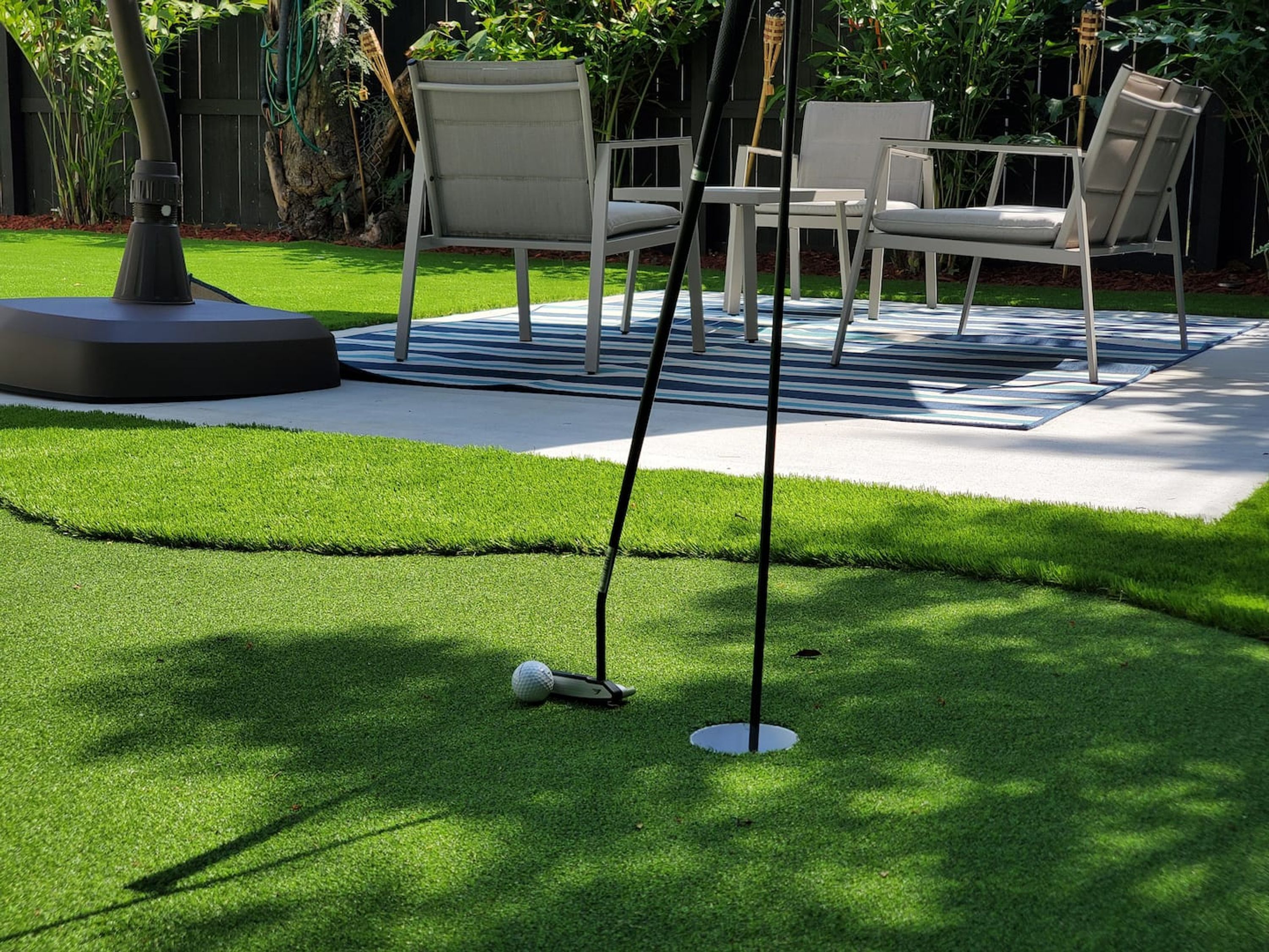 A well-maintained artificial grass lawn with a golf putting area, including a flagstick and a golf ball.