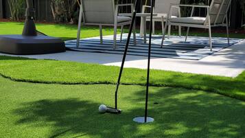 A well-maintained artificial grass lawn with a golf putting area, including a flagstick and a golf ball.