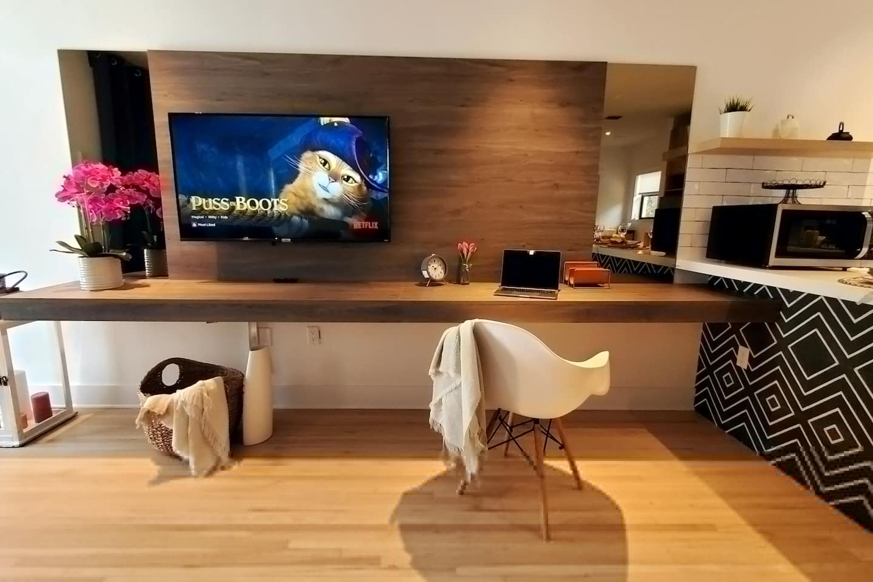 A modern kitchen with a flat-screen TV displaying 'Puss in Boots', a wooden countertop, a microwave, and a patterned backsplash.