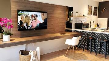 A modern kitchen with a flat-screen TV mounted on the wall, a bar area with stools, and a dining table.