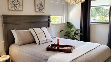 A neatly made bed with pillows, a bedside table with a lamp, and a window with a view of greenery.