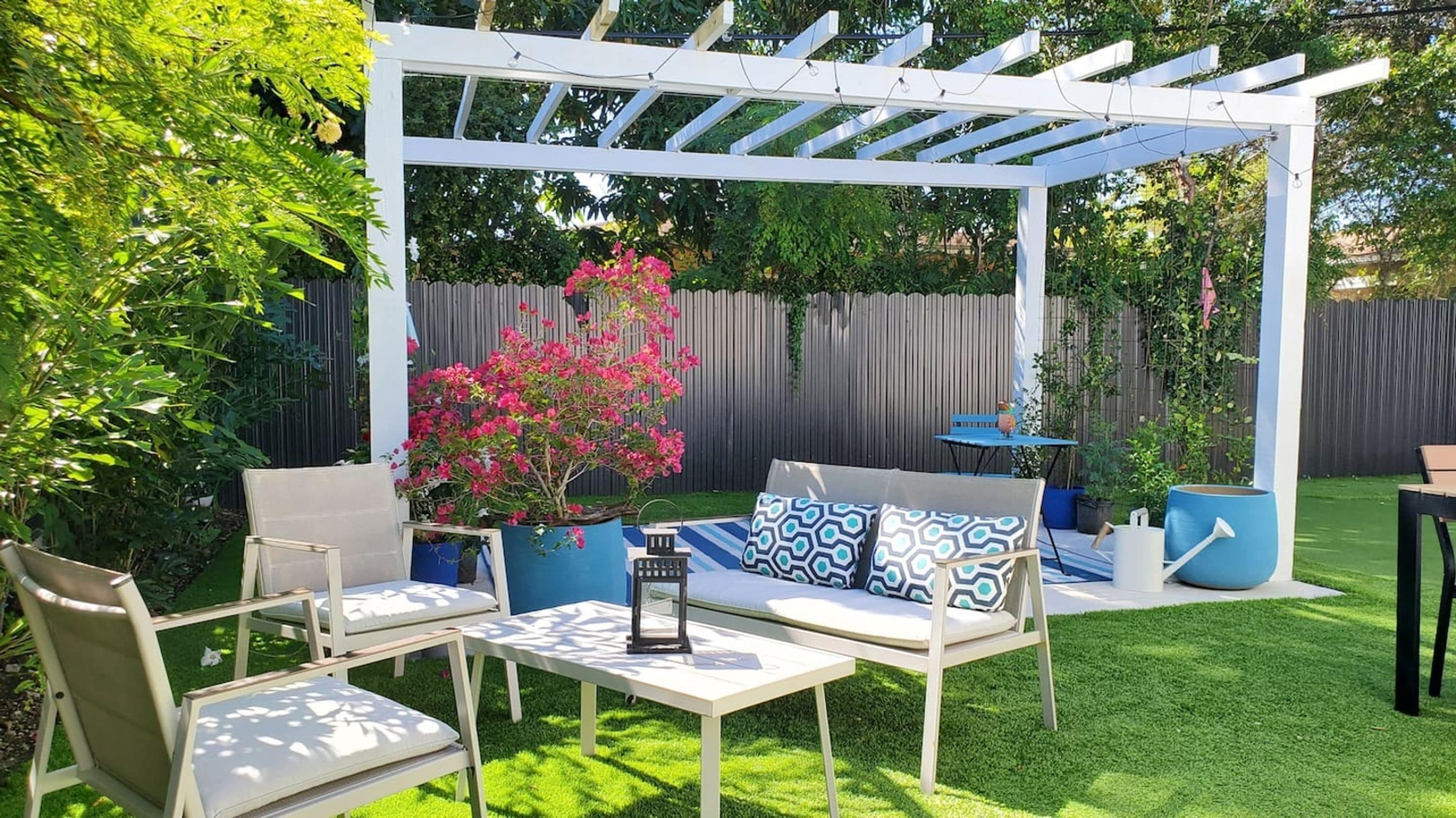 A patio with a white pergola, outdoor furniture, and a potted plant.