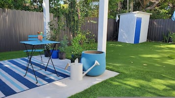 A backyard with a blue table and chairs, a large planter, and a shed.