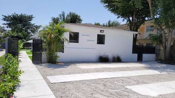 A modern building with a white facade, a gravel driveway, and a gated entrance.