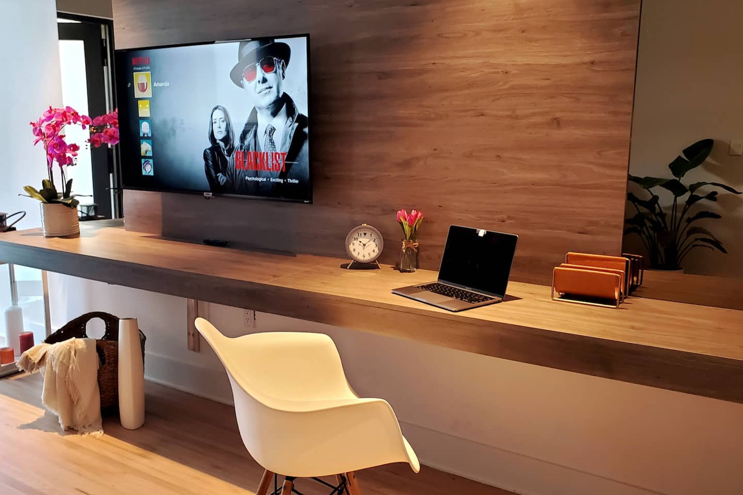A modern reception desk with a flat-screen TV displaying a movie, a laptop, a clock, and a vase of flowers.