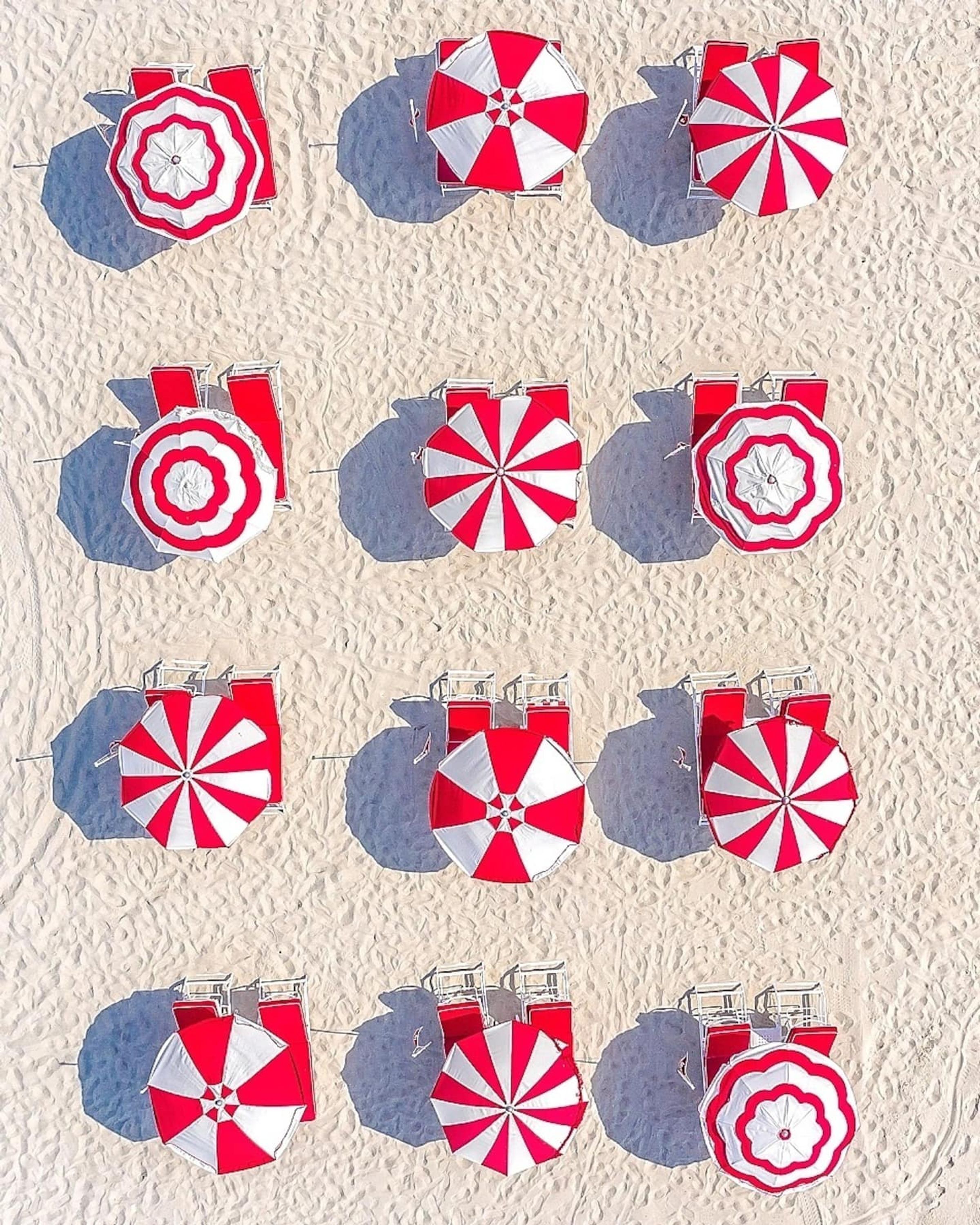 Ein Strand mit mehreren roten und weißen gestreiften Sonnenschirmen und Liegestühlen.