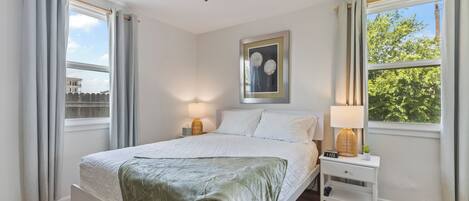 A bedroom with a bed, two bedside tables, a ceiling fan, and a window with curtains.