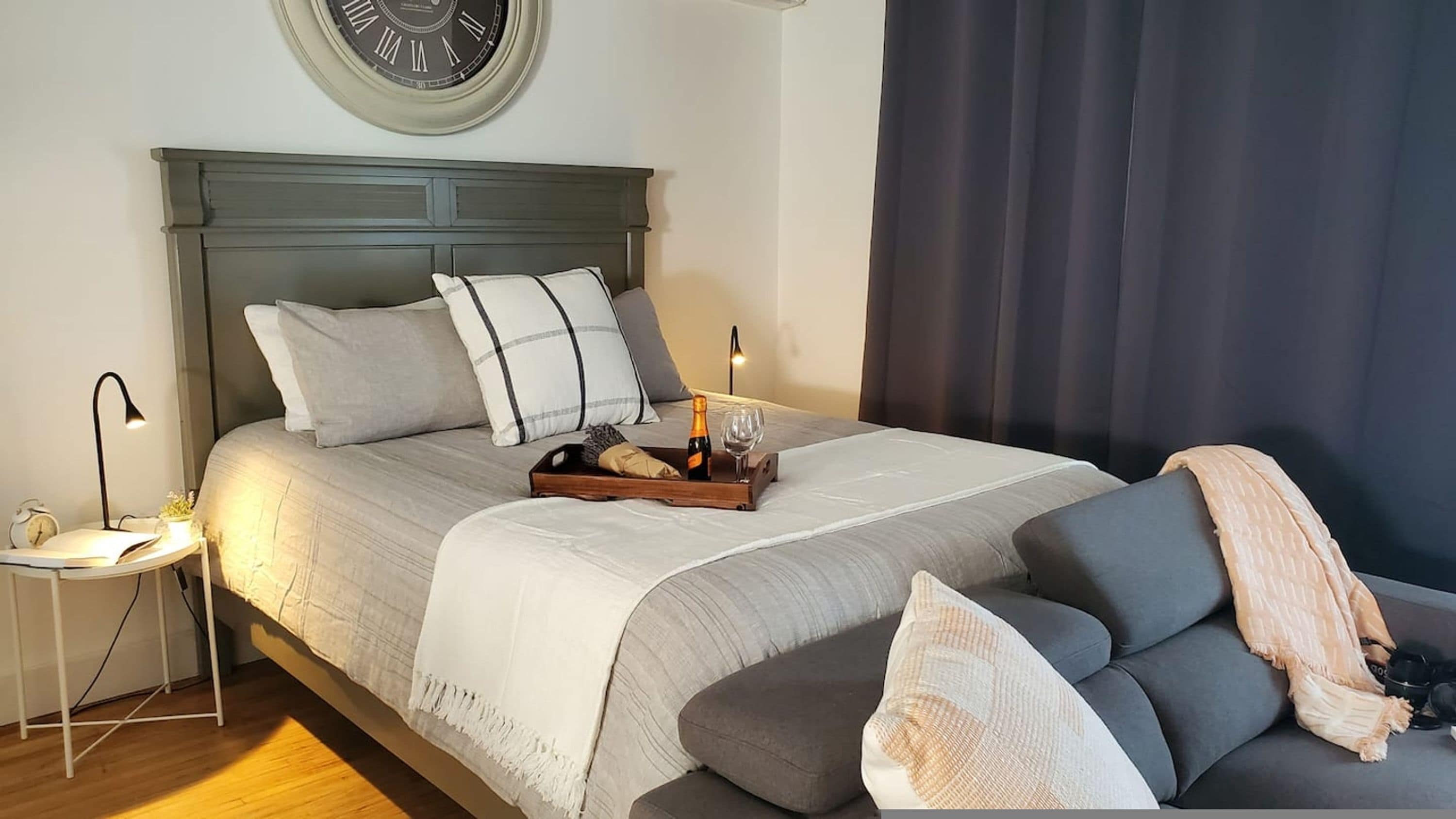 Ein ordentlich bezogenes Bett mit einem Holztischchen, Kissen und einer Champagnerflasche.