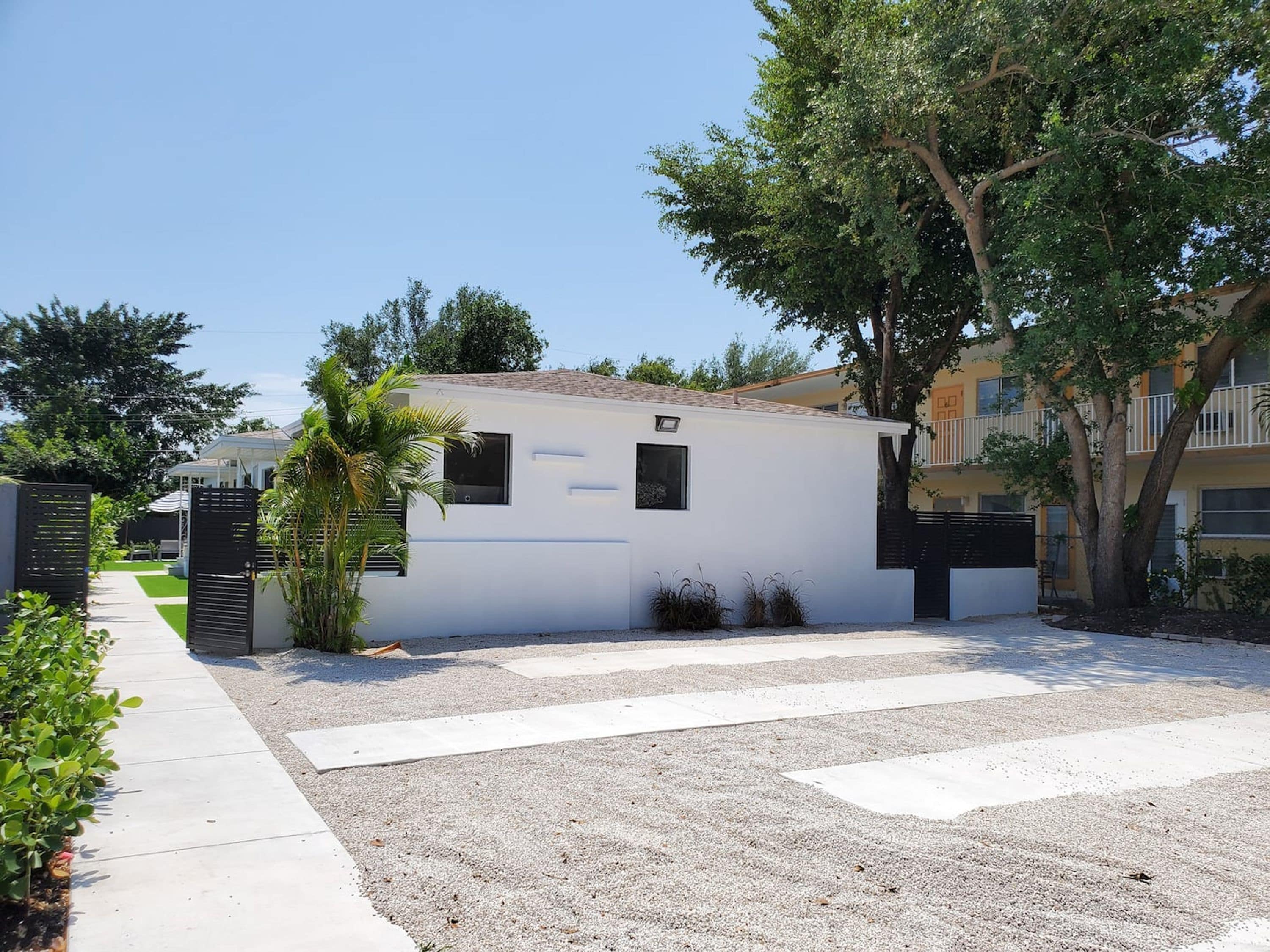 A modern white building with a flat roof, surrounded by a gravel driveway and a concrete pathway.