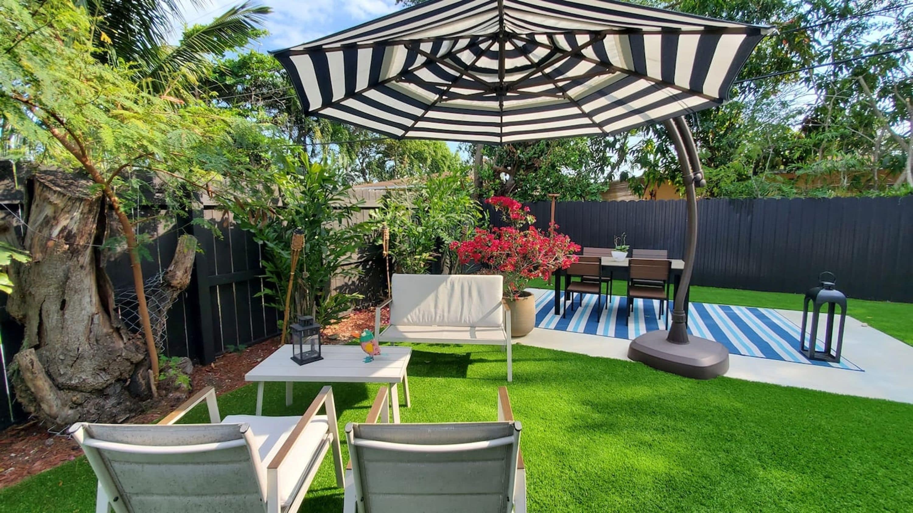 Ein Garten mit Terrasse, Tisch, Stühlen, Sonnenschirm, einem kleinen Gartenbeet und einem Zaun.