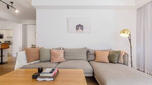 Een moderne woonkamer met een modulaire bank, een houten salontafel met boeken, een vloerlamp en een lijst met een afbeelding aan de muur.