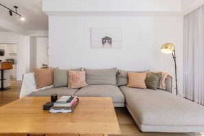 A modern living room with a sectional sofa, a wooden coffee table with books, a floor lamp, and a framed picture on the wall. - Raleigh Escape Urban Comfort near Albert Park Lake (Windsor)