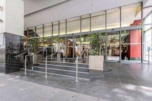 Ein moderner Gebäudeeingang mit Glastüren, einer Treppe und Metallgeländern.