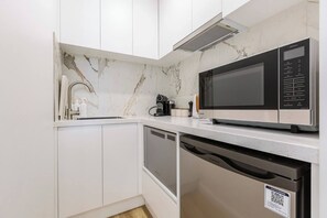 A modern kitchen with white cabinetry, a built-in microwave, and a dishwasher. - Yarra Edge River and Skyline Views with Shared Pool (Melbourne)