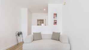 A minimalist living room with a light-colored sofa, a small side table, and a coat rack. - Yarra Edge River and Skyline Views with Shared Pool (Melbourne)